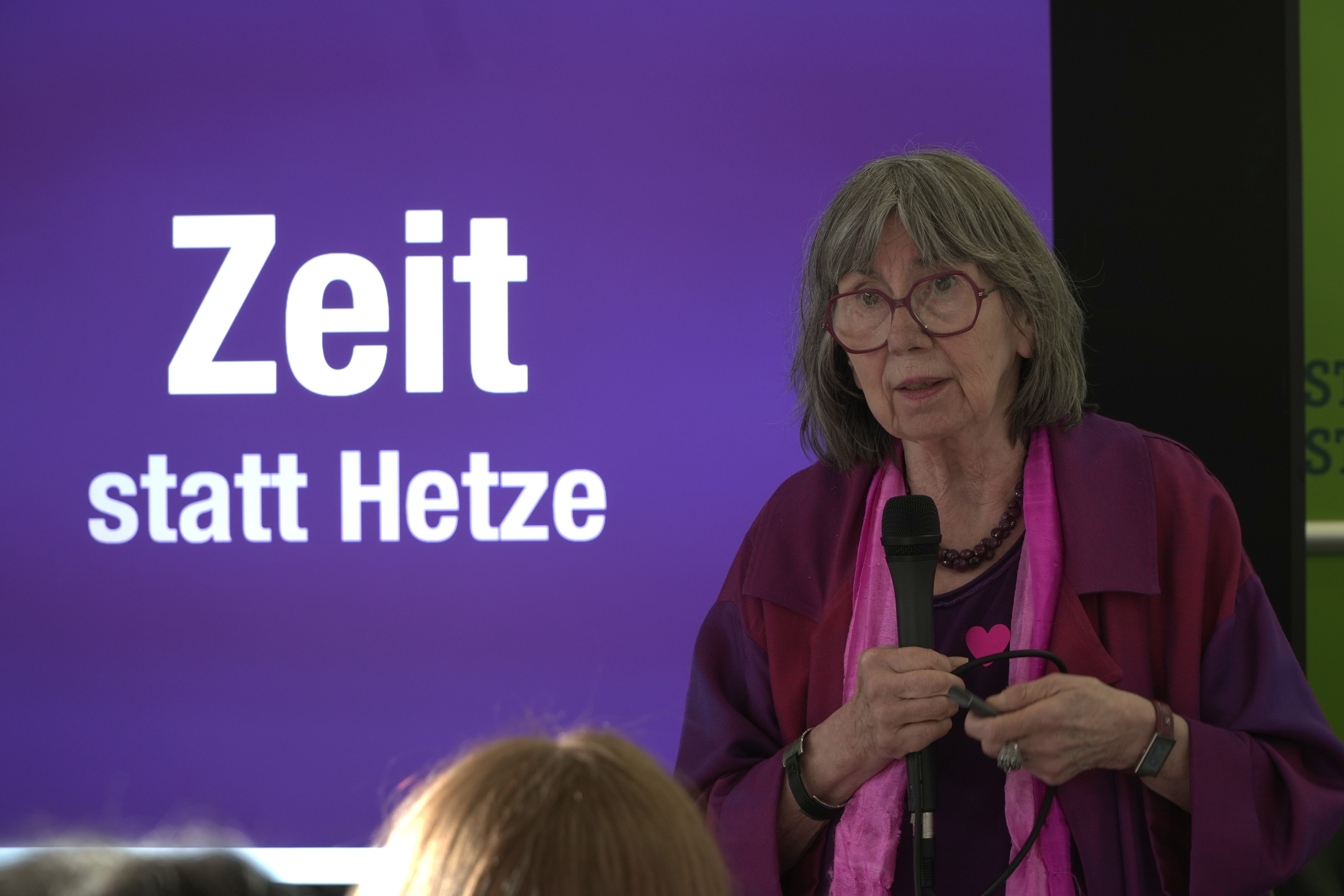 Rednerin auf der Bühne vor einem Banner mit der Aufschrift „Zeit statt Hetze“
